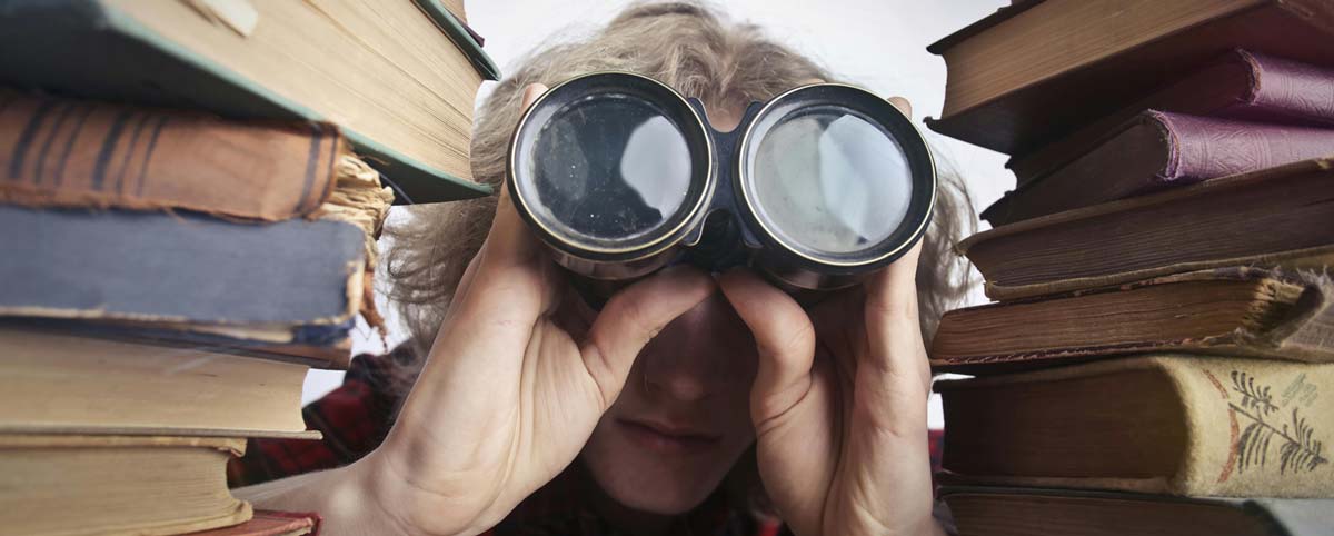A man using binoculars between old books